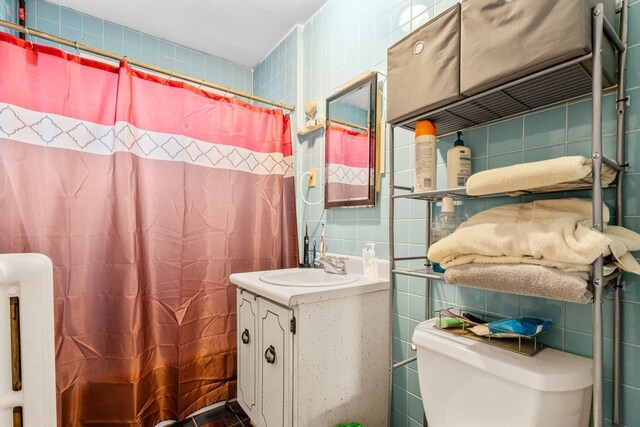 bathroom with toilet, walk in shower, vanity, and tile walls