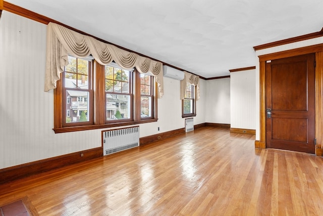 unfurnished living room featuring light hardwood / wood-style floors, a wall unit AC, radiator heating unit, and plenty of natural light