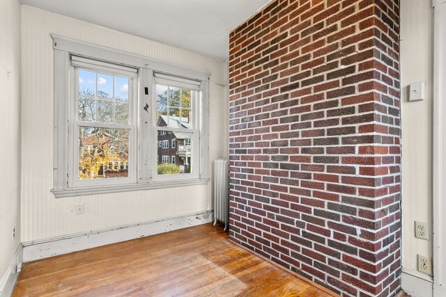 unfurnished room featuring brick wall, radiator heating unit, and light wood-type flooring