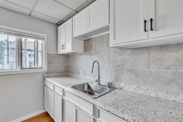 kitchen featuring tasteful backsplash, white cabinets, sink, light hardwood / wood-style floors, and a drop ceiling