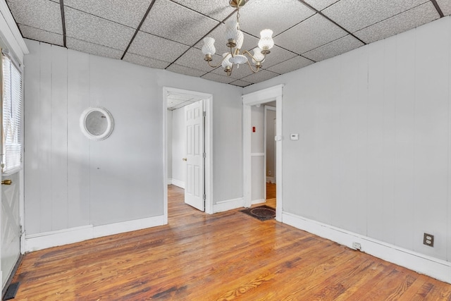 spare room featuring a notable chandelier, a drop ceiling, a healthy amount of sunlight, and hardwood / wood-style flooring