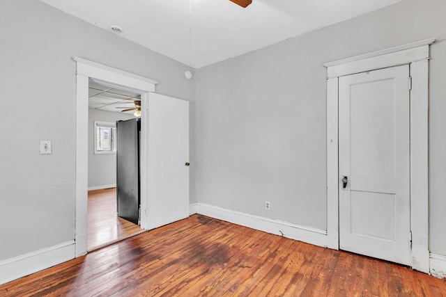 unfurnished bedroom with black fridge, wood-type flooring, a closet, and ceiling fan