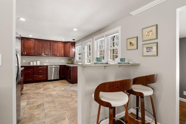 kitchen featuring appliances with stainless steel finishes, a breakfast bar, sink, kitchen peninsula, and light stone countertops