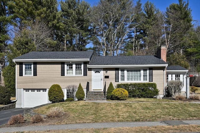 tri-level home featuring roof with shingles, driveway, a chimney, a front lawn, and a garage