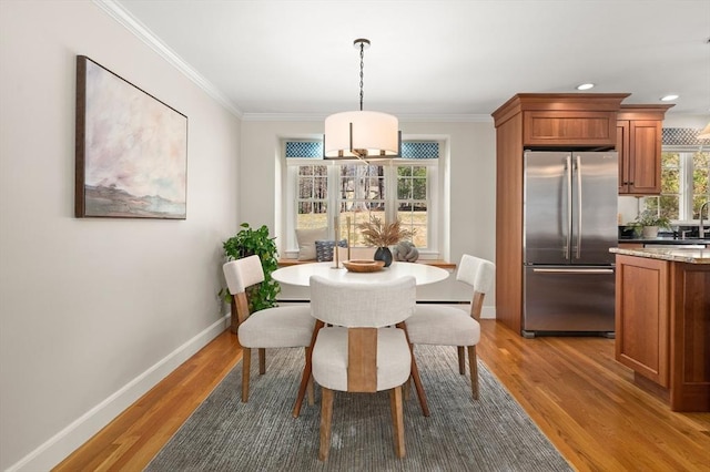 dining space featuring crown molding, baseboards, and light wood finished floors