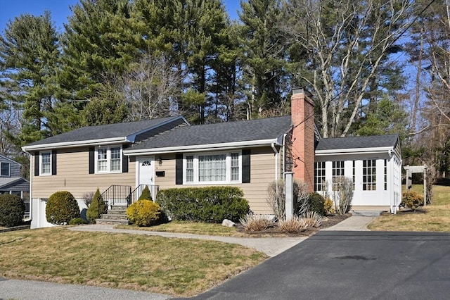 tri-level home with a chimney, a front lawn, and roof with shingles