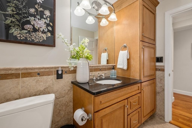 half bathroom featuring toilet, wood finished floors, tile walls, wainscoting, and vanity