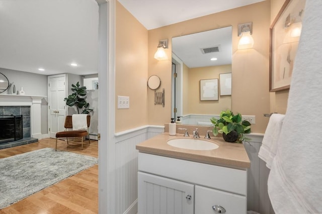 bathroom featuring vanity, wood finished floors, visible vents, a fireplace, and wainscoting