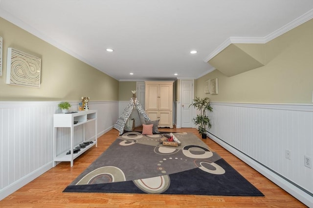 living area featuring a baseboard heating unit, light wood-style floors, a wainscoted wall, and crown molding