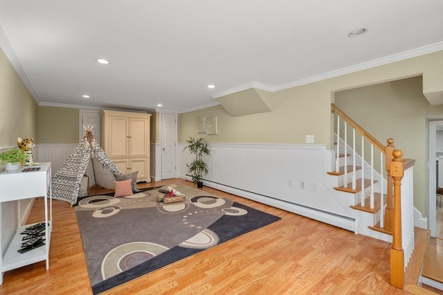 sitting room with stairway, light wood-type flooring, ornamental molding, baseboard heating, and wainscoting