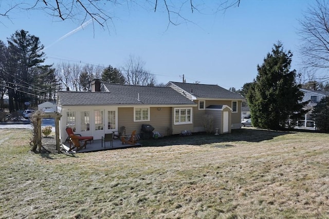 rear view of property with a chimney, a yard, and a shingled roof