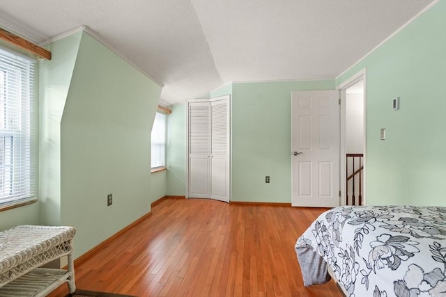 bedroom with lofted ceiling, a closet, light wood-style floors, a textured ceiling, and baseboards