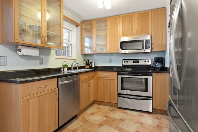 kitchen with tasteful backsplash, dark stone countertops, stone finish flooring, stainless steel appliances, and a sink