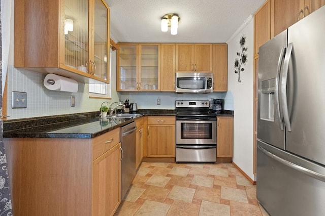 kitchen featuring a textured ceiling, stainless steel appliances, a sink, tasteful backsplash, and glass insert cabinets