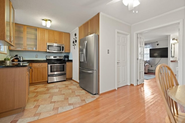 kitchen featuring glass insert cabinets, stainless steel appliances, crown molding, light wood-type flooring, and a sink