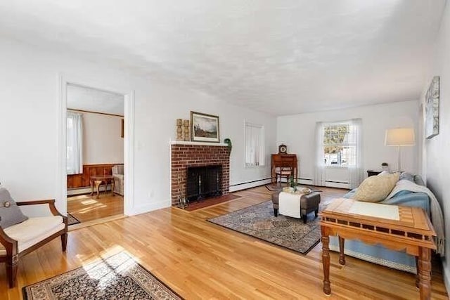 living room with a brick fireplace, light wood-style floors, and a baseboard radiator