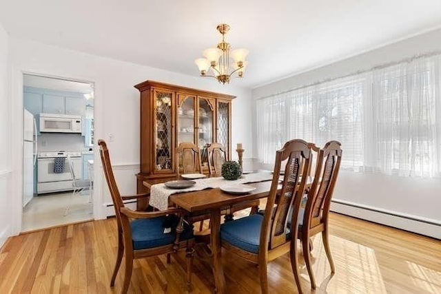 dining space with a baseboard heating unit, a notable chandelier, and light wood-style flooring