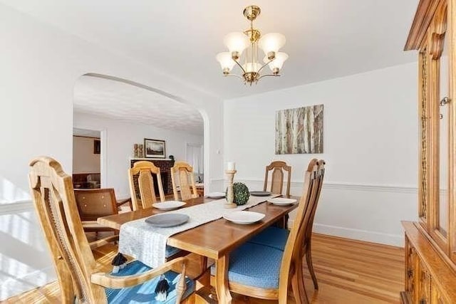 dining area with baseboards, arched walkways, light wood finished floors, and a chandelier