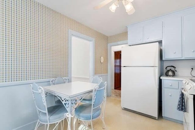 kitchen with range with electric cooktop, wallpapered walls, wainscoting, freestanding refrigerator, and a ceiling fan