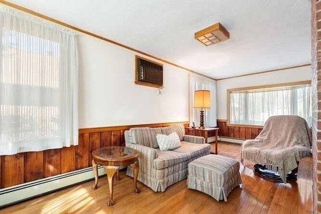 sitting room with an AC wall unit, ornamental molding, hardwood / wood-style flooring, wainscoting, and a baseboard radiator