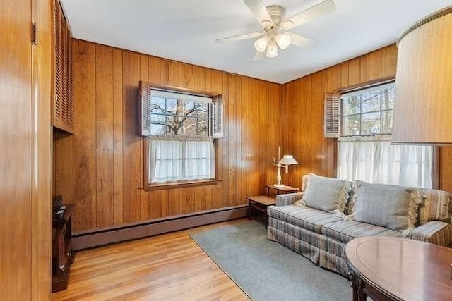 living area featuring wooden walls, ceiling fan, a baseboard heating unit, and light wood-style floors