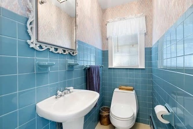 bathroom with toilet, wallpapered walls, tile walls, and a sink