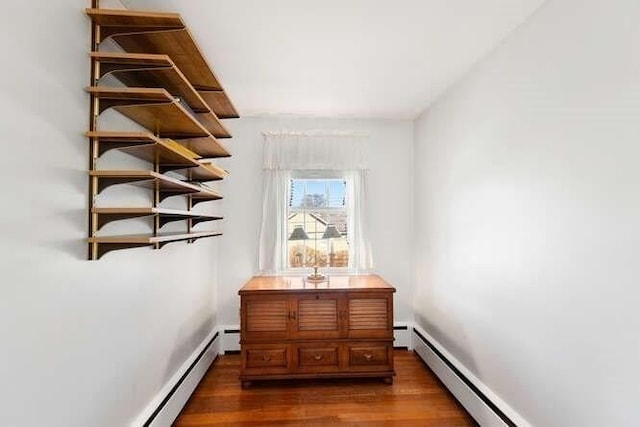 corridor with a baseboard heating unit, dark wood-type flooring, baseboard heating, and baseboards