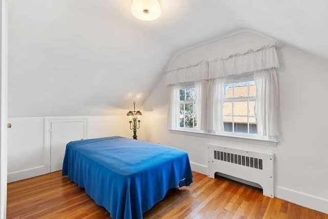 bedroom featuring vaulted ceiling, radiator heating unit, baseboards, and wood finished floors