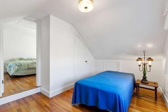 bedroom with vaulted ceiling, baseboards, and wood finished floors