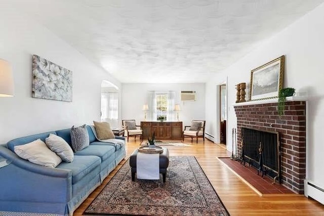 living room with a wall unit AC, a brick fireplace, wood finished floors, and baseboard heating