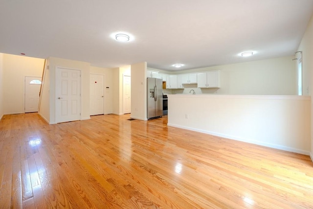 unfurnished living room featuring baseboards, light wood-style floors, and a sink