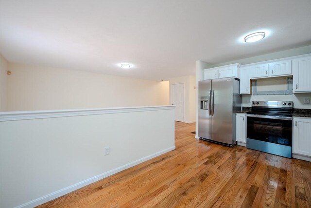 kitchen with light wood finished floors, white cabinets, baseboards, dark countertops, and appliances with stainless steel finishes