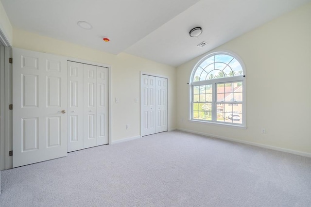 unfurnished bedroom with multiple closets, visible vents, vaulted ceiling, carpet floors, and baseboards