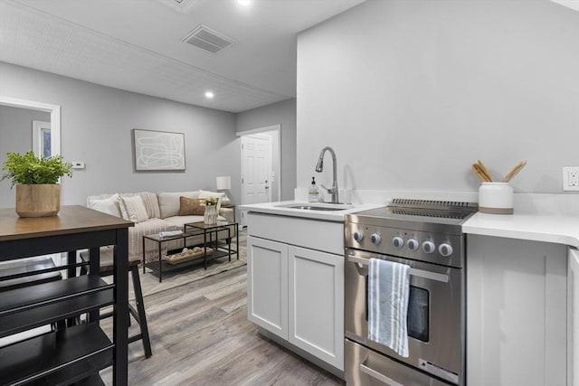 kitchen with sink, stainless steel stove, light hardwood / wood-style floors, and white cabinets