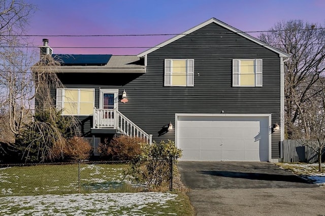 tri-level home with an attached garage, a chimney, driveway, and solar panels