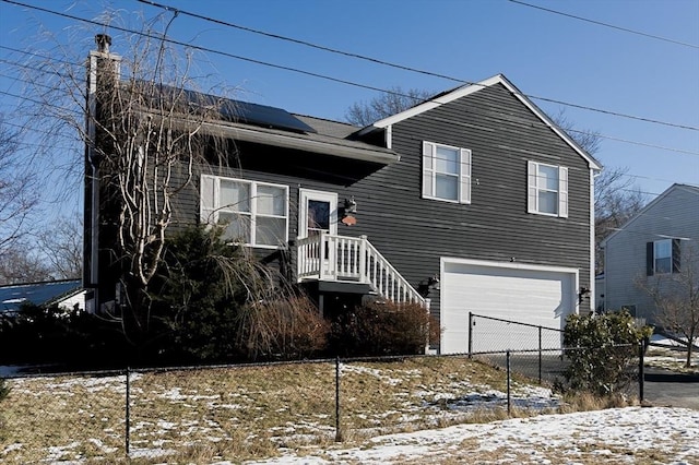 tri-level home with a chimney, solar panels, a garage, and fence
