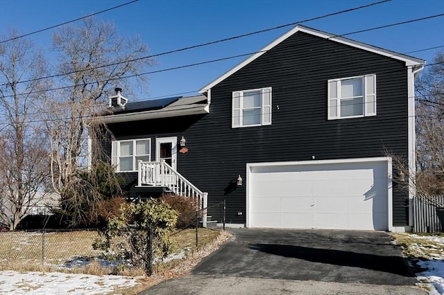 tri-level home featuring a garage, driveway, fence, solar panels, and a chimney