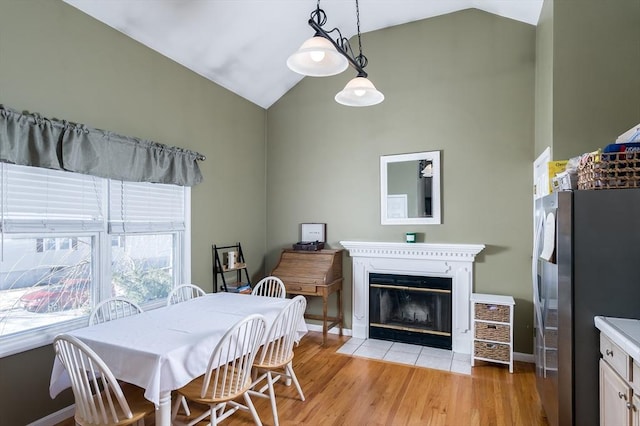 dining room with light wood-style floors, a fireplace with flush hearth, high vaulted ceiling, and baseboards