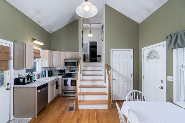 kitchen with stainless steel appliances, high vaulted ceiling, tile countertops, light wood-type flooring, and hanging light fixtures
