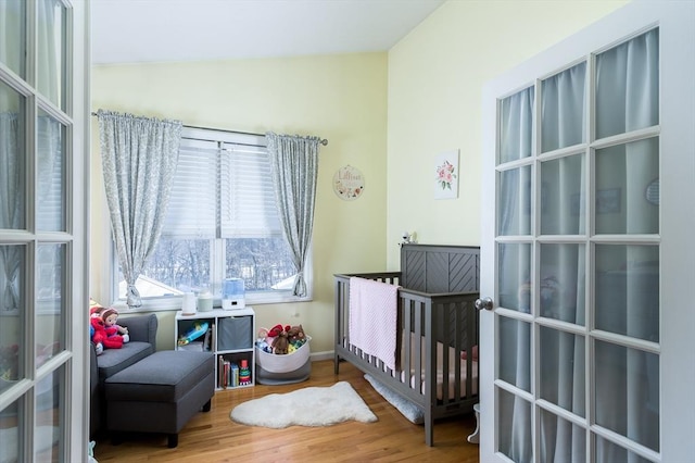 bedroom featuring a nursery area, wood finished floors, vaulted ceiling, and baseboards