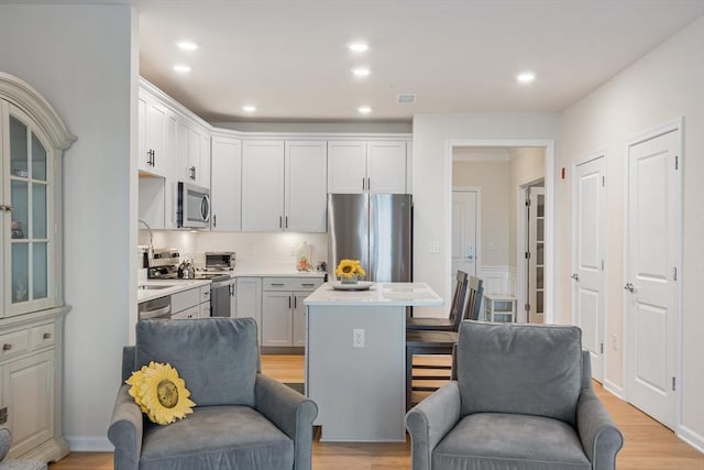 kitchen with a kitchen island, appliances with stainless steel finishes, a kitchen bar, white cabinets, and light wood-type flooring