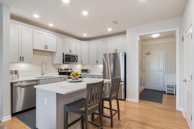 kitchen with sink, a kitchen island, appliances with stainless steel finishes, white cabinets, and light wood-type flooring