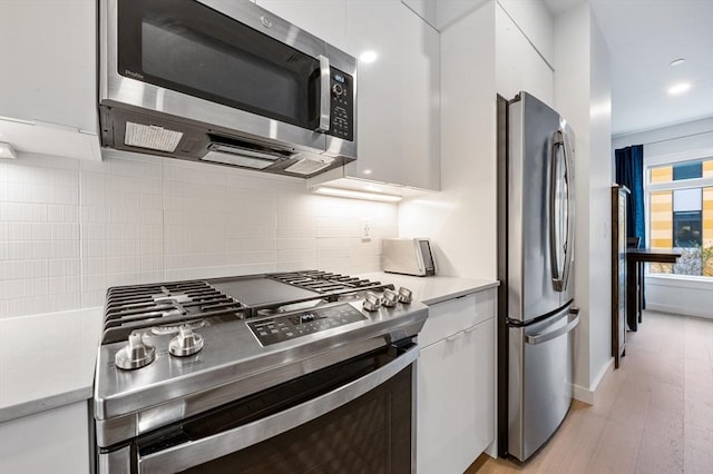 7 Lisbon St Unit 201, Boston, MA 02128 - kitchen with stainless steel appliances, light countertops, white cabinets, backsplash, and light wood-style flooring