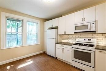 kitchen featuring white appliances, dark wood-style flooring, white cabinets, decorative backsplash, and dark countertops