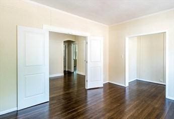 unfurnished room with baseboards, arched walkways, dark wood finished floors, and crown molding