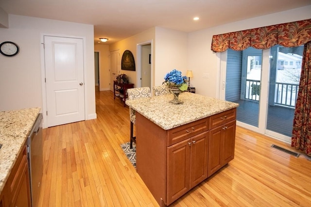 kitchen with visible vents, a center island, a breakfast bar area, light stone counters, and light wood-style floors