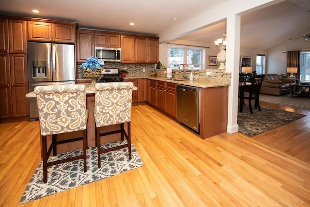 kitchen featuring backsplash, light stone counters, light wood-style floors, stainless steel appliances, and a sink