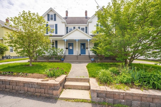 view of front facade featuring covered porch, a front lawn, and a chimney