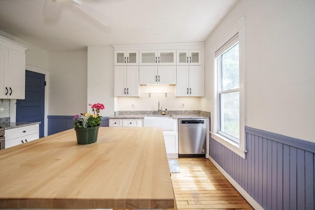 kitchen with dishwasher, a sink, wainscoting, healthy amount of natural light, and white cabinets