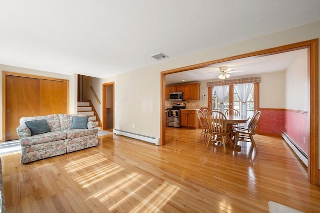 living area featuring wainscoting, light wood-style flooring, baseboard heating, and stairs